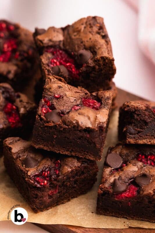 Small batch raspberry brownies cut into squares and piled on a wood cutting board.