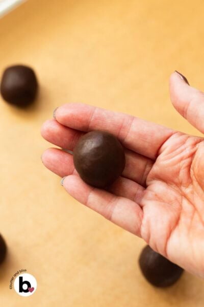 Hand rolling chocolate thumbprint cookie dough into a ball.