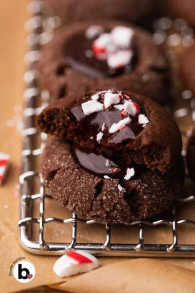 Two chocolate thumbprint cookies in stack with one cut in half and dripping glossy peppermint ganache.