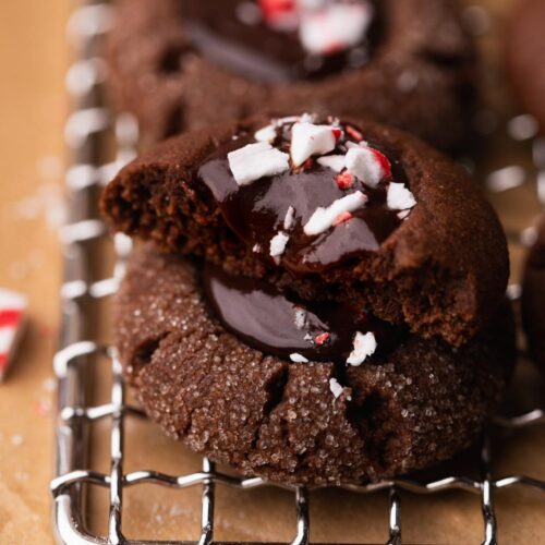 Two chocolate thumbprint cookies in stack with one cut in half and dripping glossy peppermint ganache.