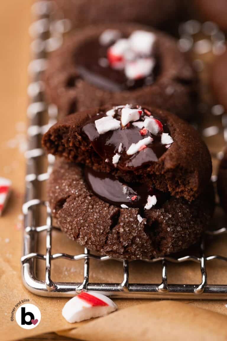 Two chocolate thumbprint cookies in stack with one cut in half and dripping glossy peppermint ganache.