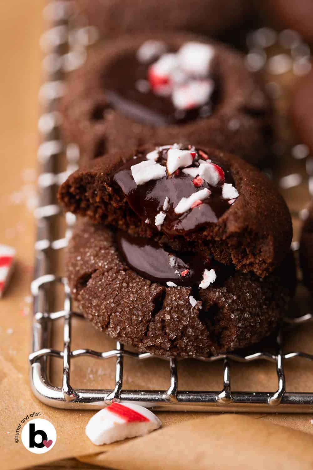 Two chocolate thumbprint cookies in stack with one cut in half and dripping glossy peppermint ganache.