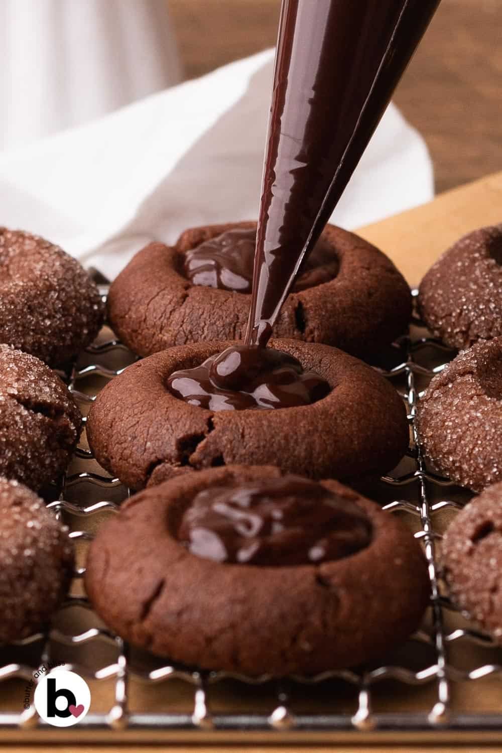 Chocolate peppermint ganache being piped into a small batch of chocolate thumbprint cookies.