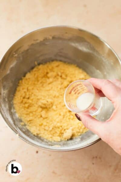 A couple splashes of milk added to sugar cookie dough in a mixing bowl to make it thick and pliable.