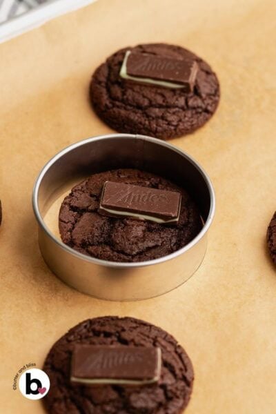 Swirling a freshly baked chocolate mint cookie around the inside of a cookie cutter to make it perfectly round.