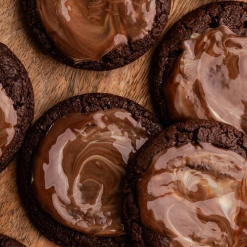 Chocoalte andes cookies with a melty candy swirled on top on a wood plate.