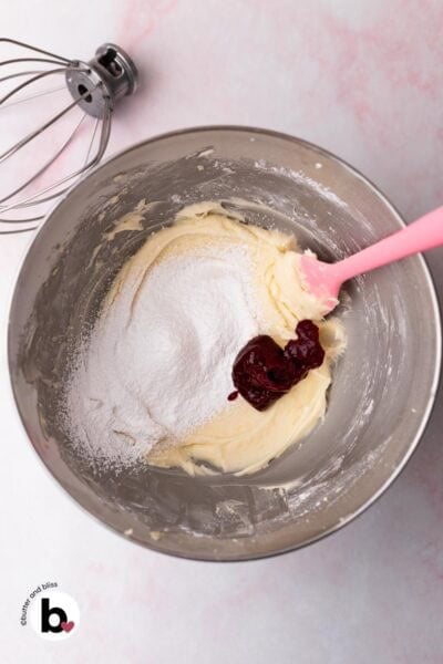 Creamed butter with sprinkled powdered sguar and cranberry sauce in a mixing bowl.