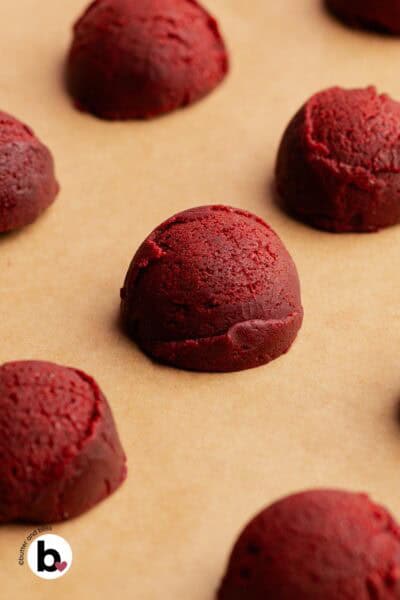 Pretty red velvet cookie dough balls on a baking sheet, ready to be baked.