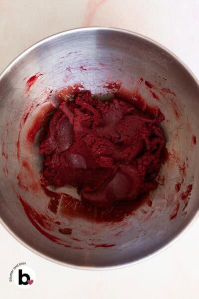 Red tinted cookie dough in a mixing bowl.