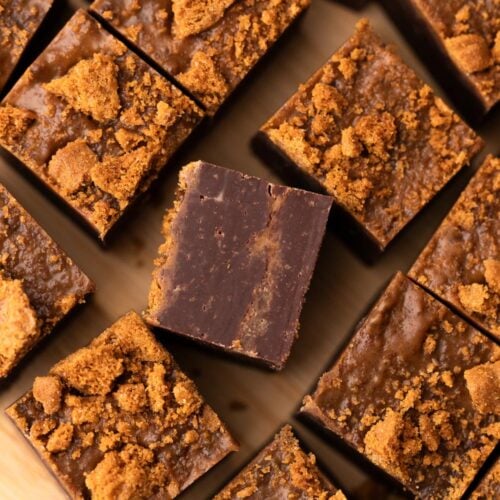Biscoff cookie butter fudge topped with cookie crumbs, cut into small squares on a cutting board.