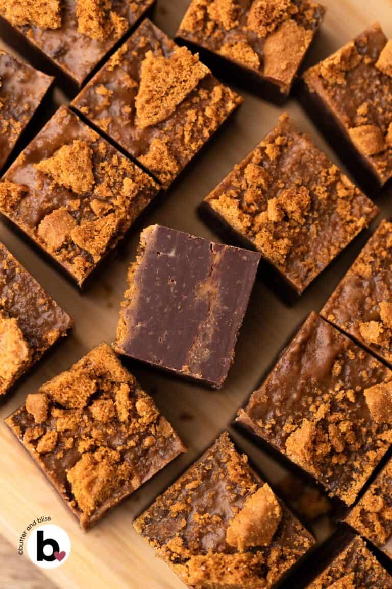 Biscoff cookie butter fudge topped with cookie crumbs, cut into small squares on a cutting board.