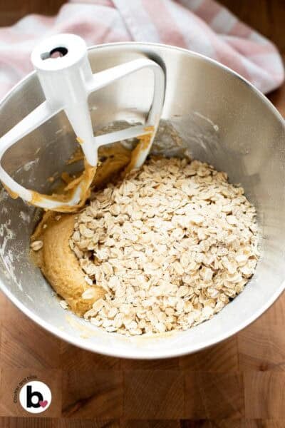 Rolled oats added to oatmeal cookie dough in a mixing bowl.