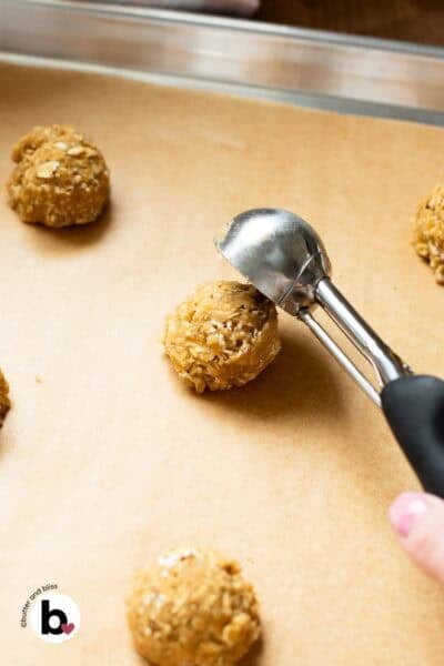 Cookie scoop portioning an oatmeal cookie dough ball onto a baking sheet.