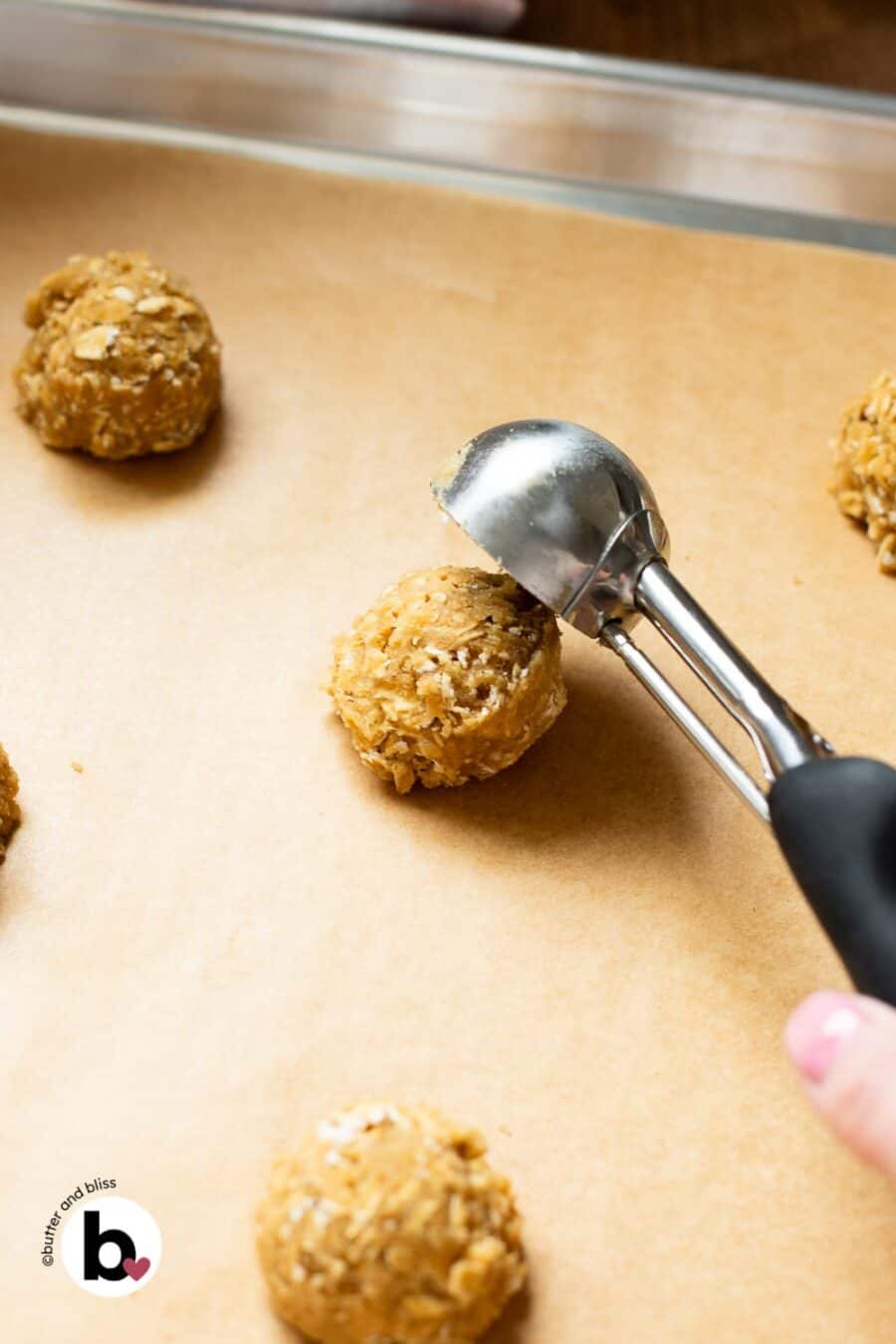 Cookie scoop portioning an oatmeal cookie dough ball onto a baking sheet.