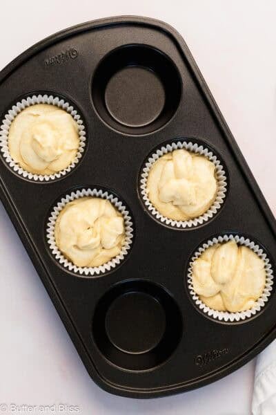 Small batch of lemon cupcake batter added to cupcake liners in a pan.