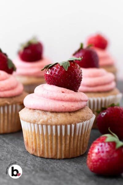 Small batch of strawberry cupcakes with strawberry frosting arranged on a table.