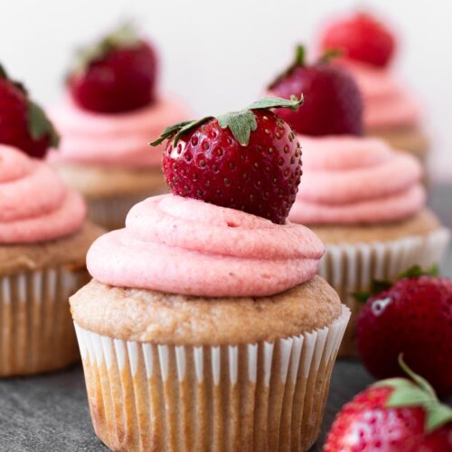 Small batch of strawberry cupcakes with strawberry frosting arranged on a table.