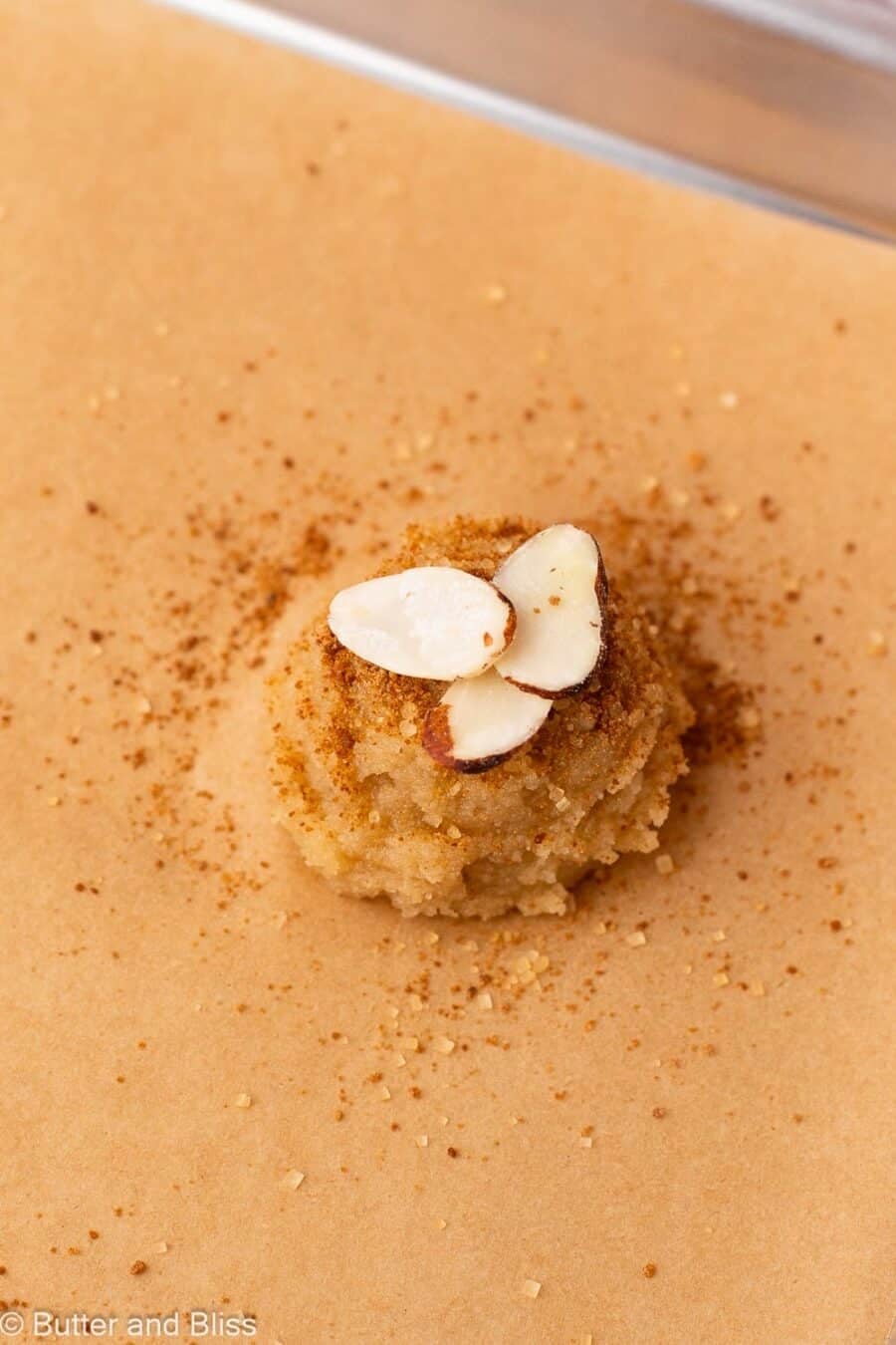Almond and maple cookie dough scoop topped with sugar and almond slices on a baking sheet.