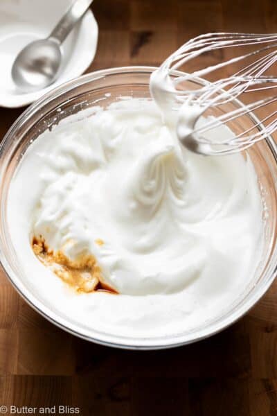 Beaten egg whites in a mixing bowl with vanilla added.