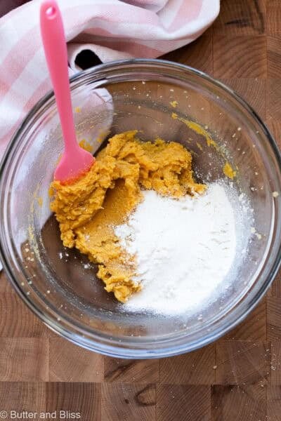 Flour added to wet cookie dough ingredients in a mixing bowl.