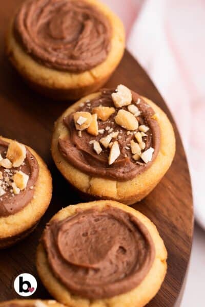 Cookie cups on a wood tray filled with light chocolate filling and topped with nuts.