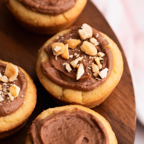 Cookie cups on a wood tray filled with light chocolate filling and topped with nuts.