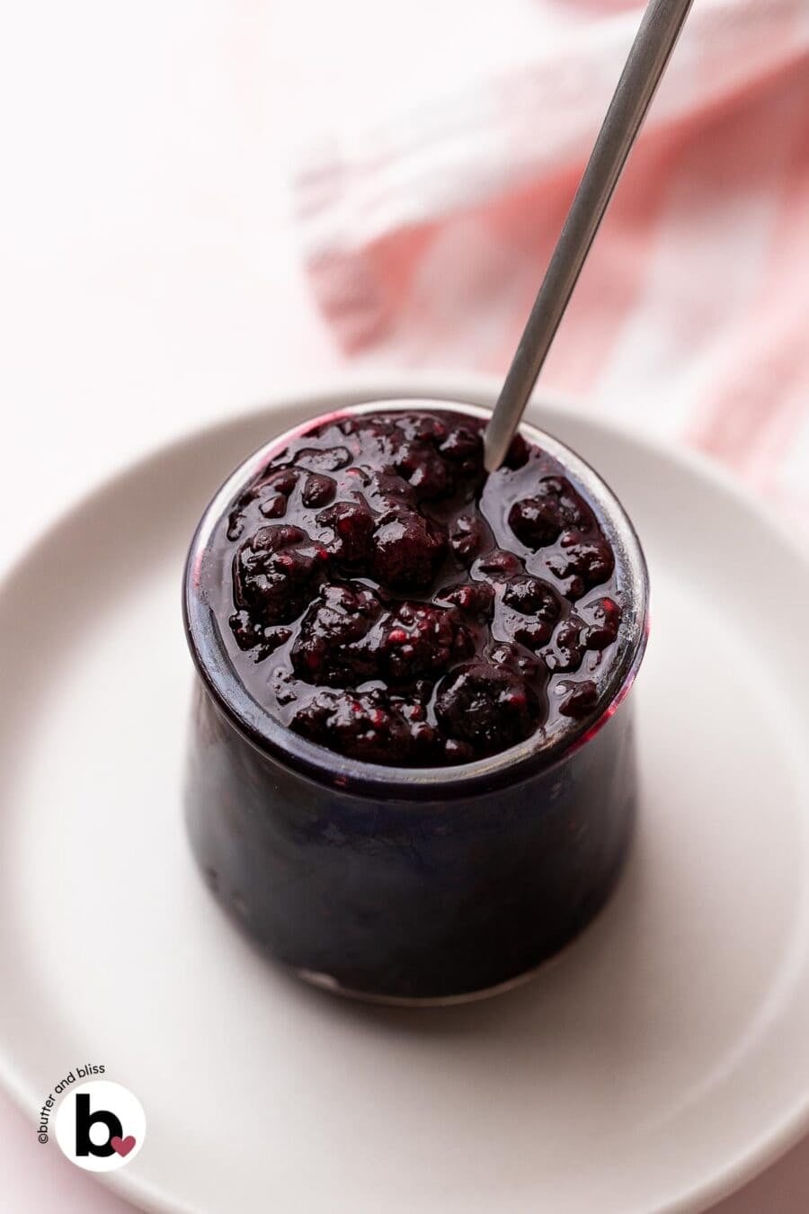 Thick berry compote in a small jar with a spoon.