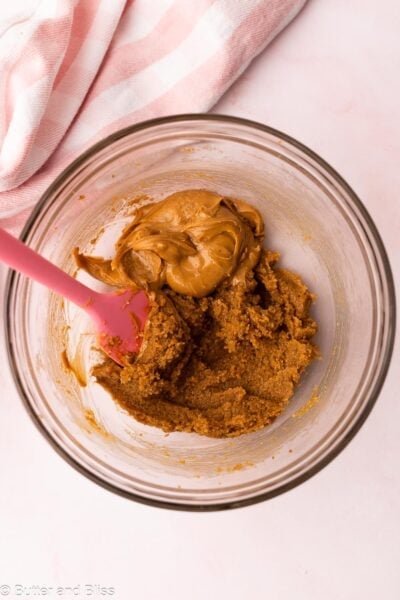 Creamy peanut butter added to a mixing bowl of creamed butter and sugar.