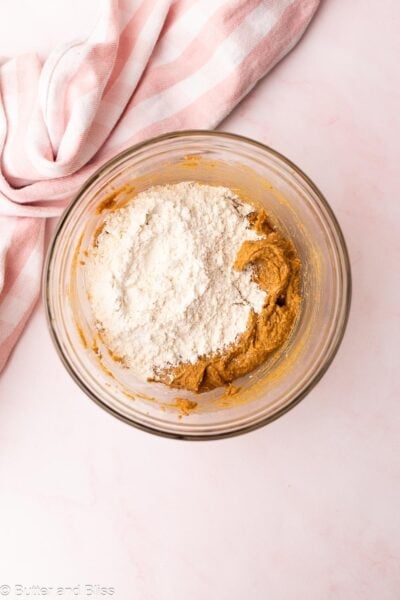 Dry ingredients added on top of wet cookie dough ingredients in a mixing bowl.