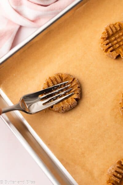Fork pressing criss-cross pattern into peanut butter cookie dough on a baking sheet.