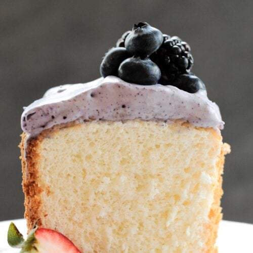 A slice of fluffy angel food cake with fresh berries and whipped cream on a plate.