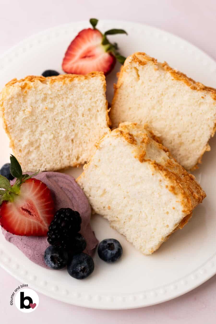 Slices of angel food cake on a white plate with berries and whipped cream.