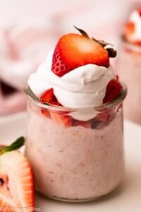 Creamy strawberr overnight oats in a glass with strawberry slices and whipped cream.