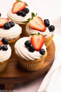 Small batch of frosted vanilla berry cupcakes on a wood plate.