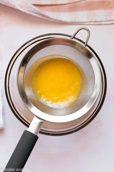 Lemon curd strained through a strainer over a bowl.