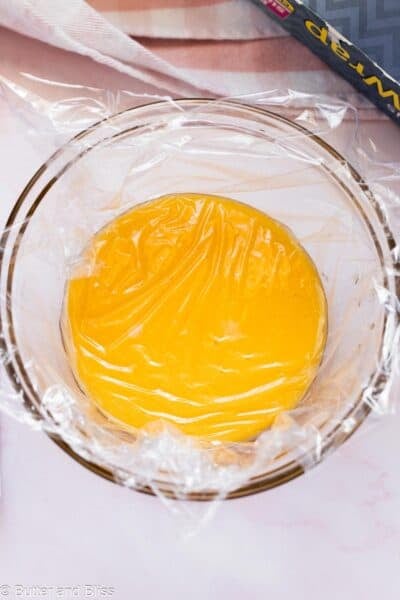 Lemon curd in a mixing bowl, covered with plastic wrap.