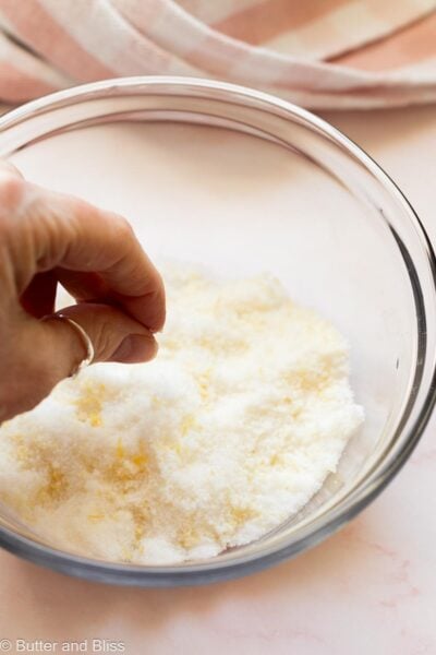Hand rubbing lemon zest into sugar.