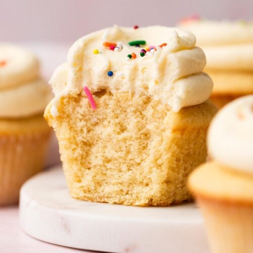 The cottony-soft inside of a vanilla cupcake with vanilla frosting, cut in half on a plate.