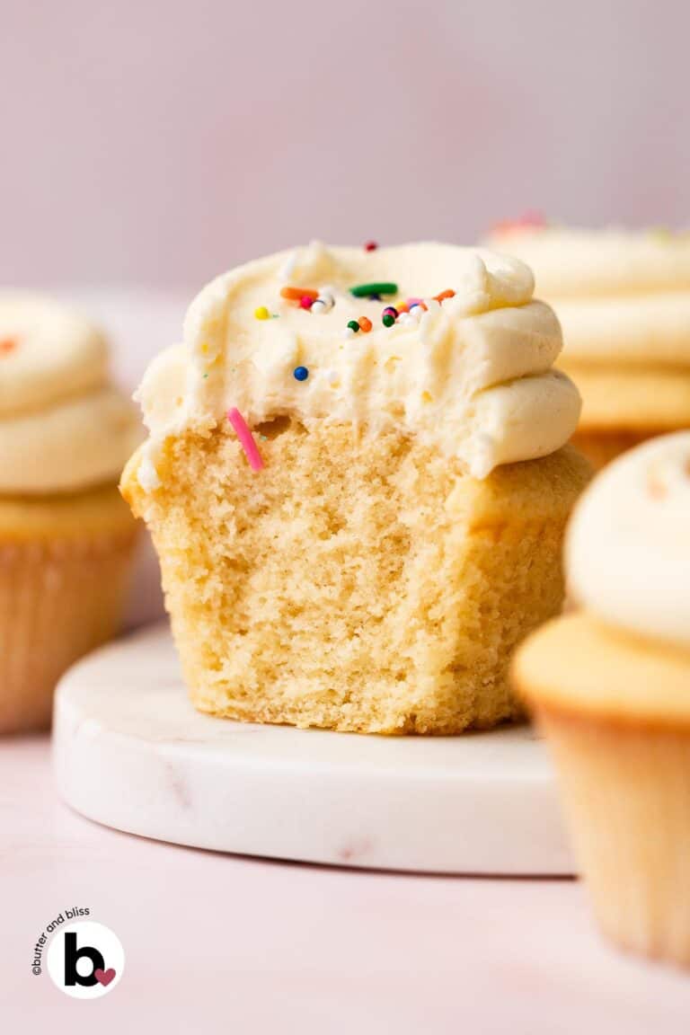 The cottony-soft inside of a vanilla cupcake with vanilla frosting, cut in half on a plate.