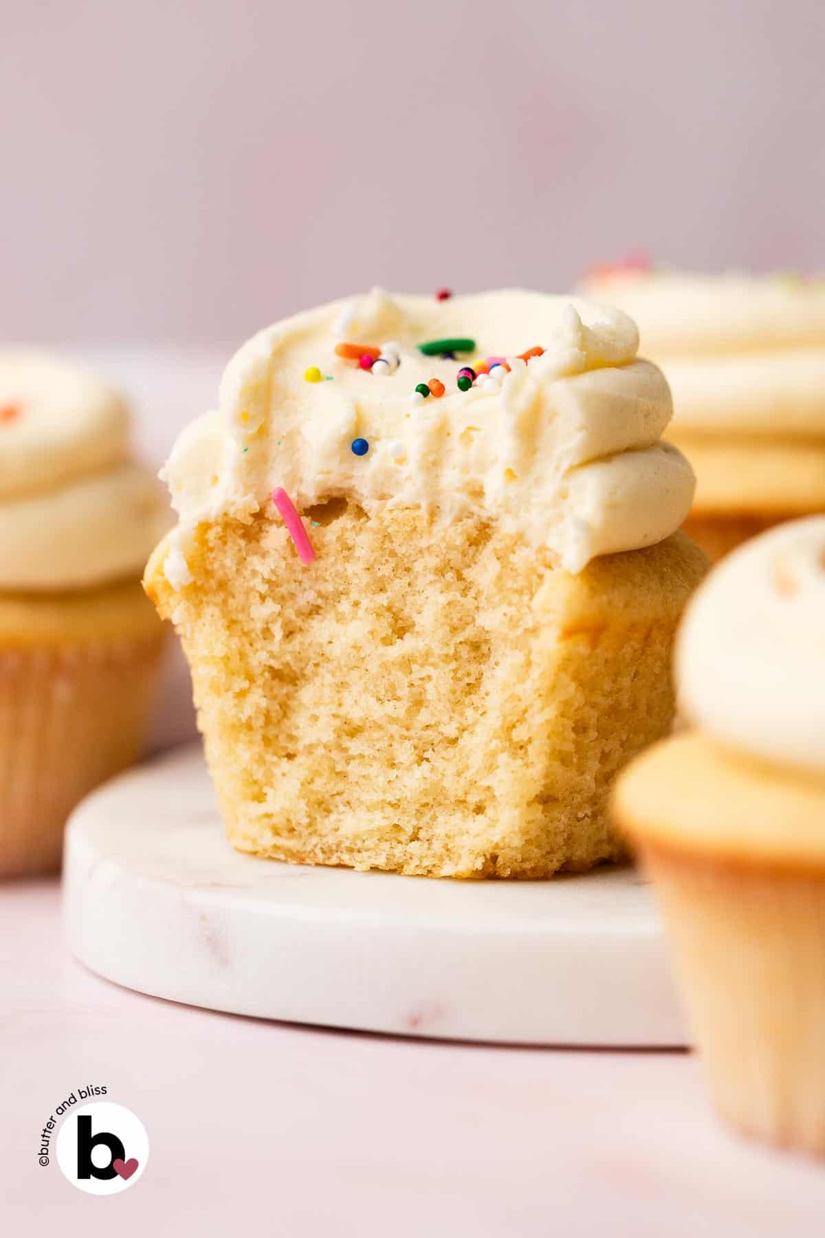 The cottony-soft inside of a vanilla cupcake with vanilla frosting, cut in half on a plate.
