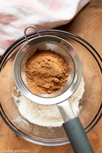 Cocoa powder sifted into a mixing bowl of flour.