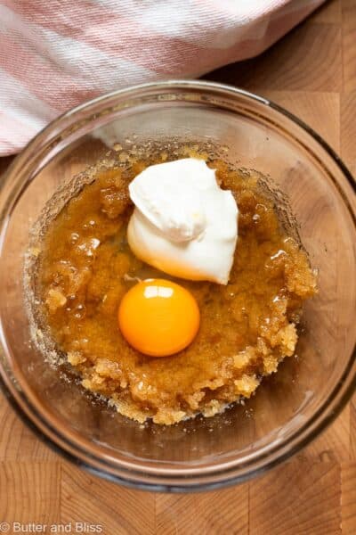 Egg and sour cream added to combined sugars in a mixing bowl.