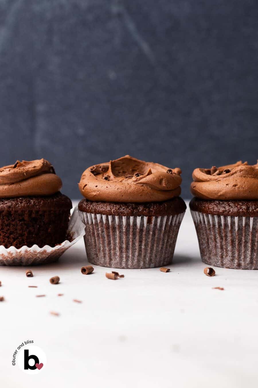 A row of three chocolate frosted chocolate cupcakes on a table.
