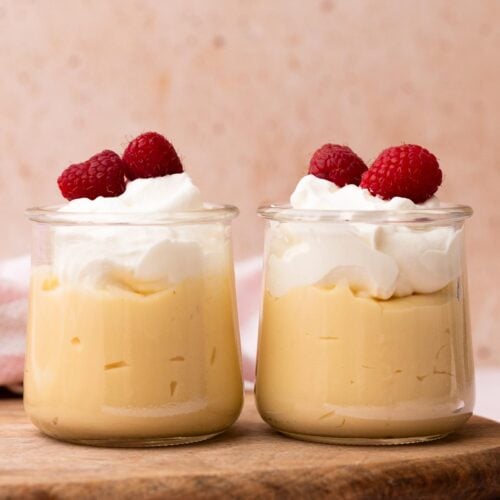 Two small jars of vanilla pudding topped with whipped cream and berries.