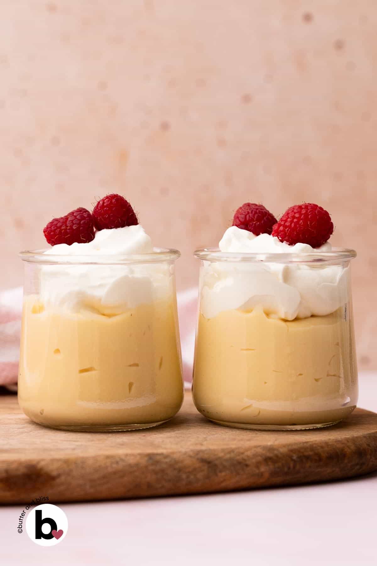 Two small jars of vanilla pudding topped with whipped cream and berries.