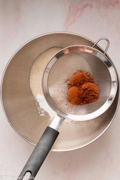 Cocoa powder sifted over a bowl of flour.