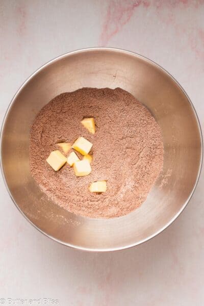 Butter cubes added to chocolate dry ingredients in a bowl.