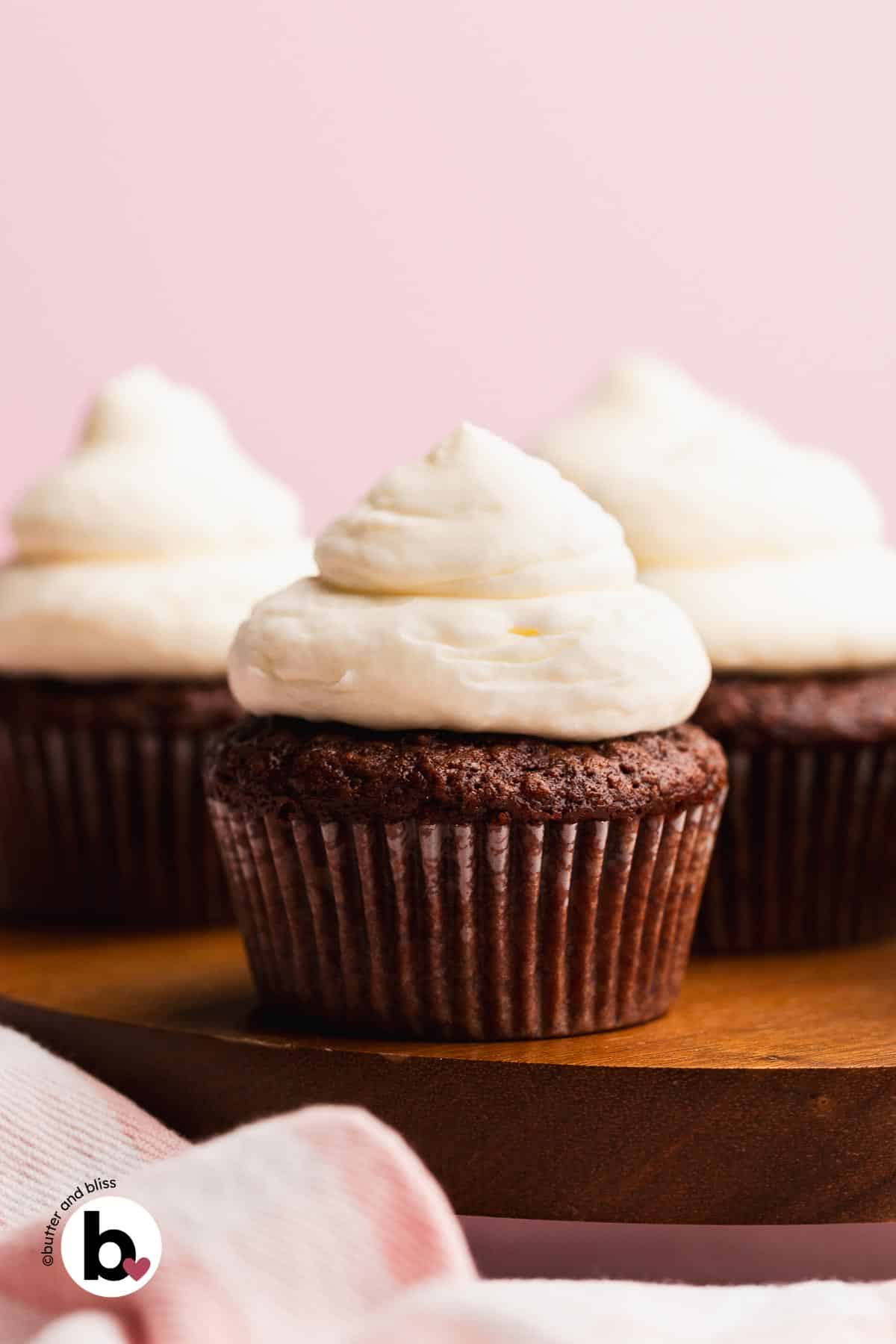 Small batch of chocolate eggless cupcakes with white frosting on a wood plate.