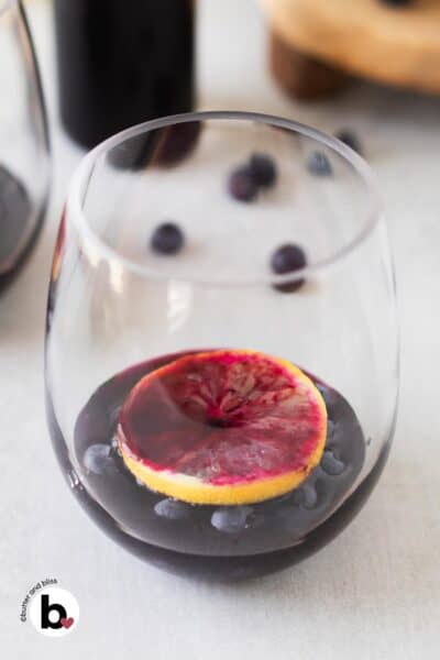 Blueberry syrup poured over a lemon slice and blueberries in a glass.