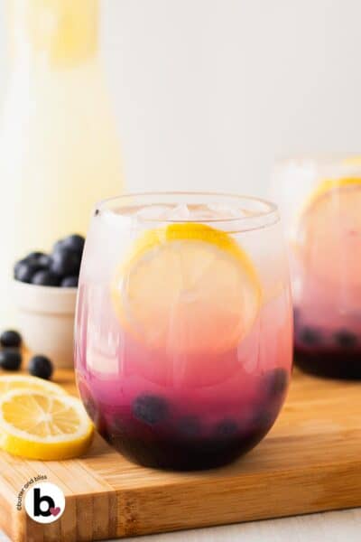 Pretty blueberry lemonade in a glass with lemon wedge and fresh blueberry garnish.